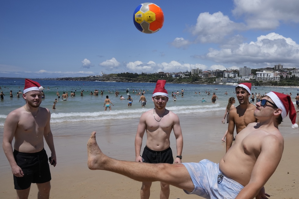 Ragazzi con cappellini da Babbo Natale giocano a pallone a Bondi Beach
