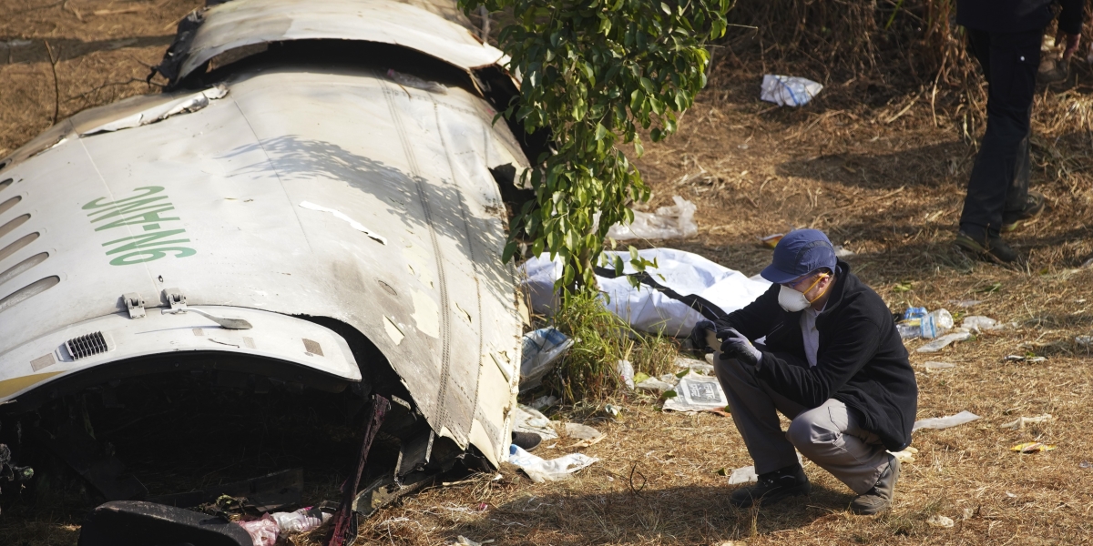 un uomo chino di fianco ai rottami di un aereo in un prato