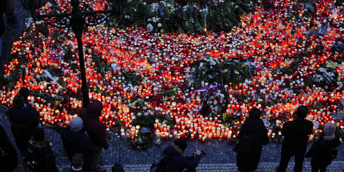 Delle persone accendono delle candele davanti alla facoltà di Filosofia dell'Università Carolina a Praga dopo l'attacco del 21 dicembre 2023 (AP Photo/Petr David Josek)