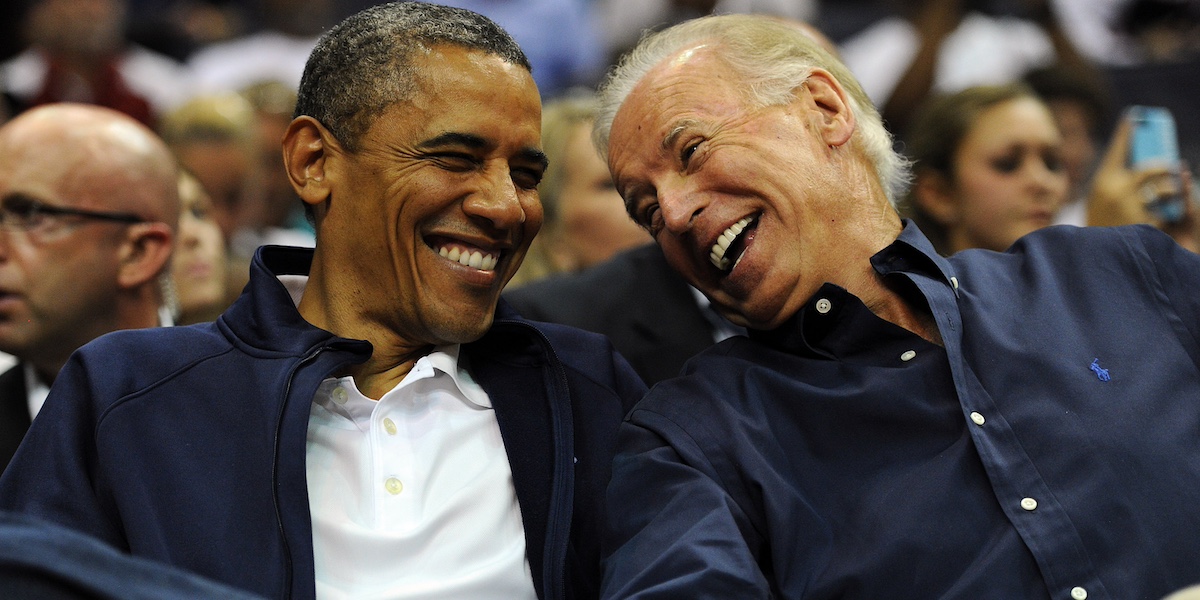 L’ex presidente degli Stati Uniti Barack Obama e l’allora vicepresidente Joe Biden, seduti vicino, ridono mentre assistono a una partita di basket