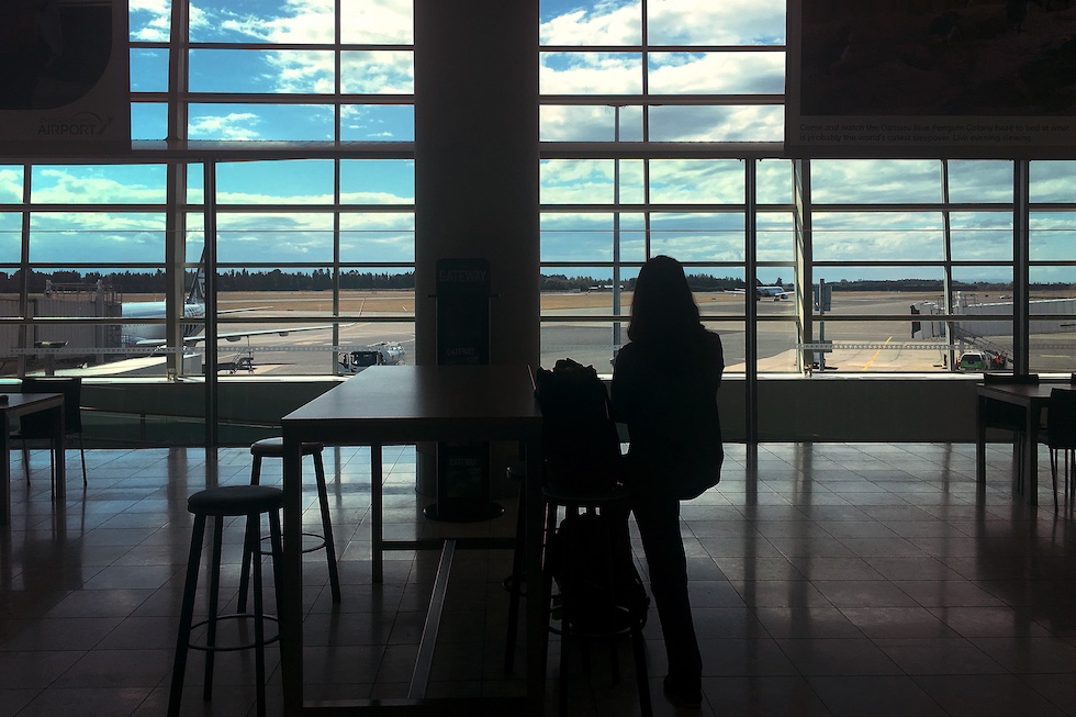 una donna in attesa da sola in un aeroporto osserva gli aerei all'esterno