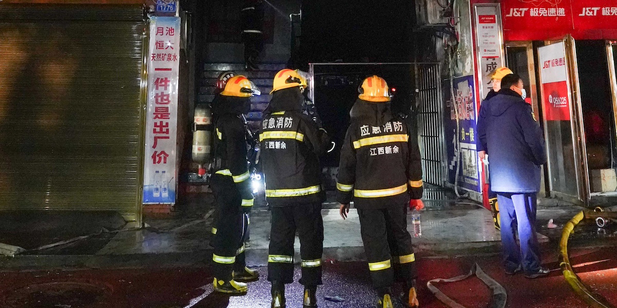 Tre vigili del fuoco davanti all'entrata del negozio da cui è partito l'incendio completamente bruciata