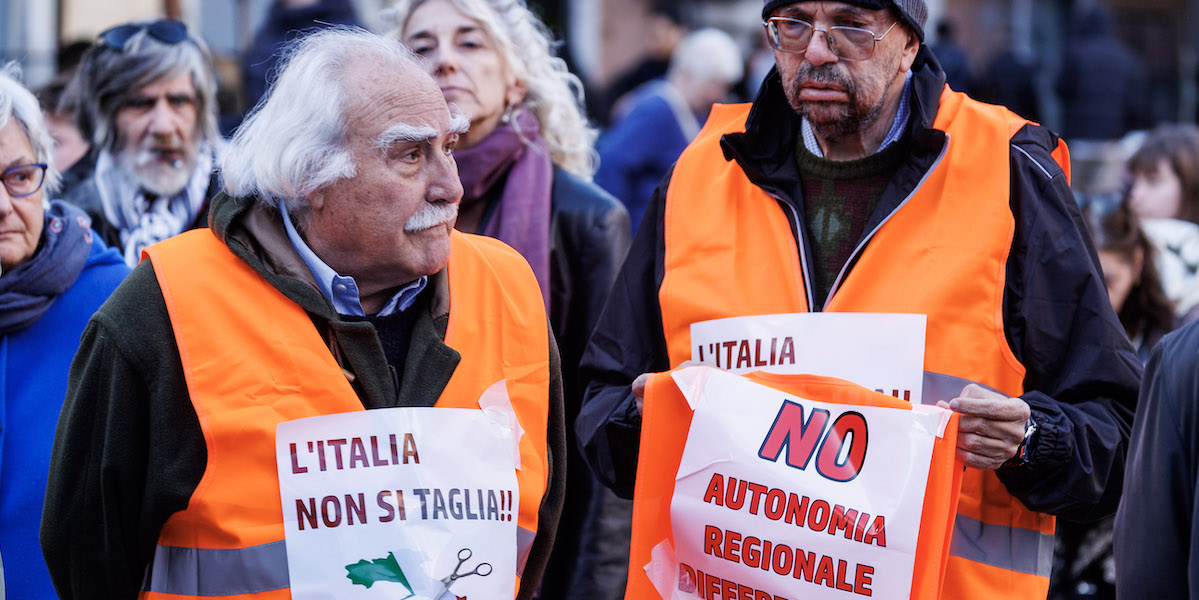 Foto di due signori con pettorina arancione e cartelli contro l'autonomia che partecipano a un presidio a Roma