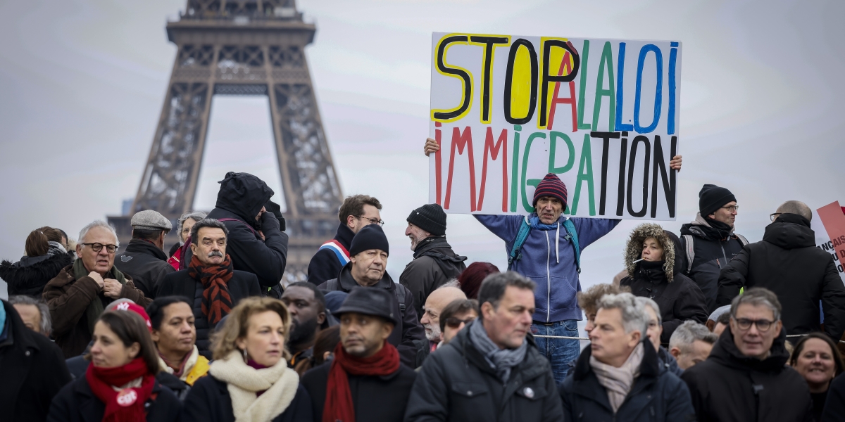 un uomo con un cartellone che dice "stop alla legge sull'immigrazione" in francese, in un gruppo di persone, davanti alla tour eiffel