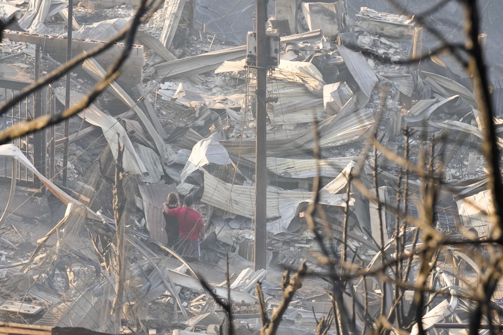 Due persone guardano i resti delle case distrutte dagli incendi