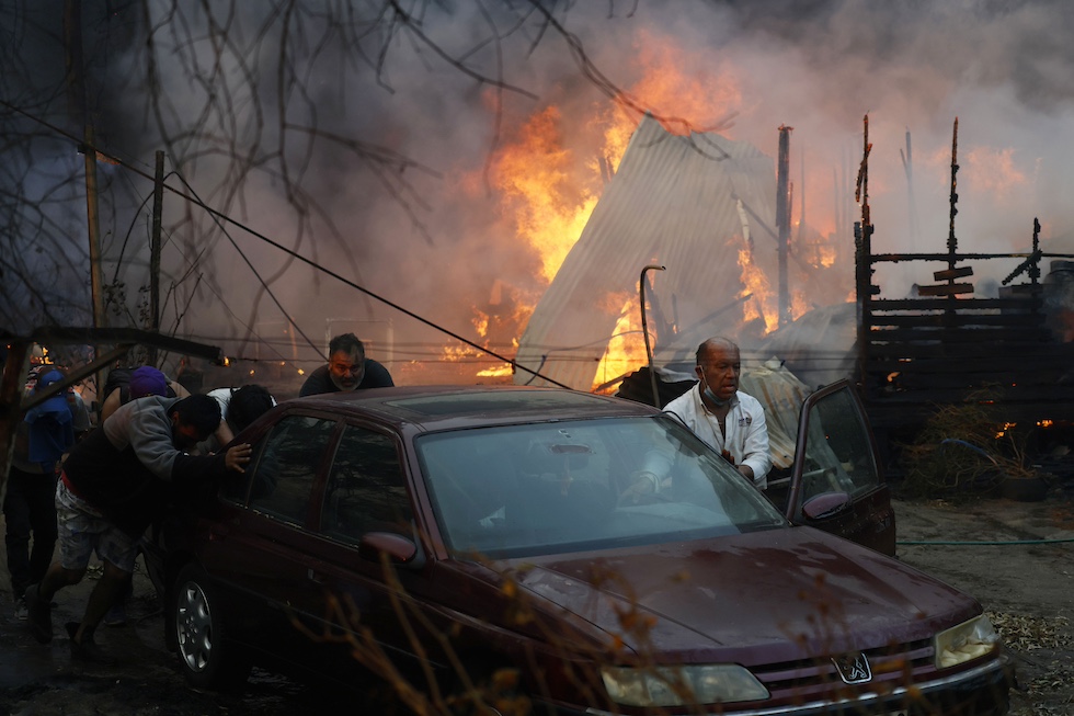 Un uomo spinge a mano una macchina con le fiamme sullo sfondo