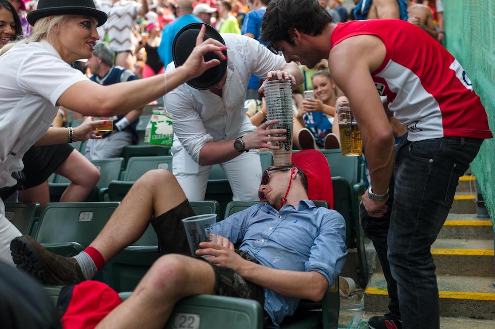 Un tifoso ubriaco sugli spalti durante una partita di rugby, e gli amici che gli impilano in testa dei bicchieri vuoti