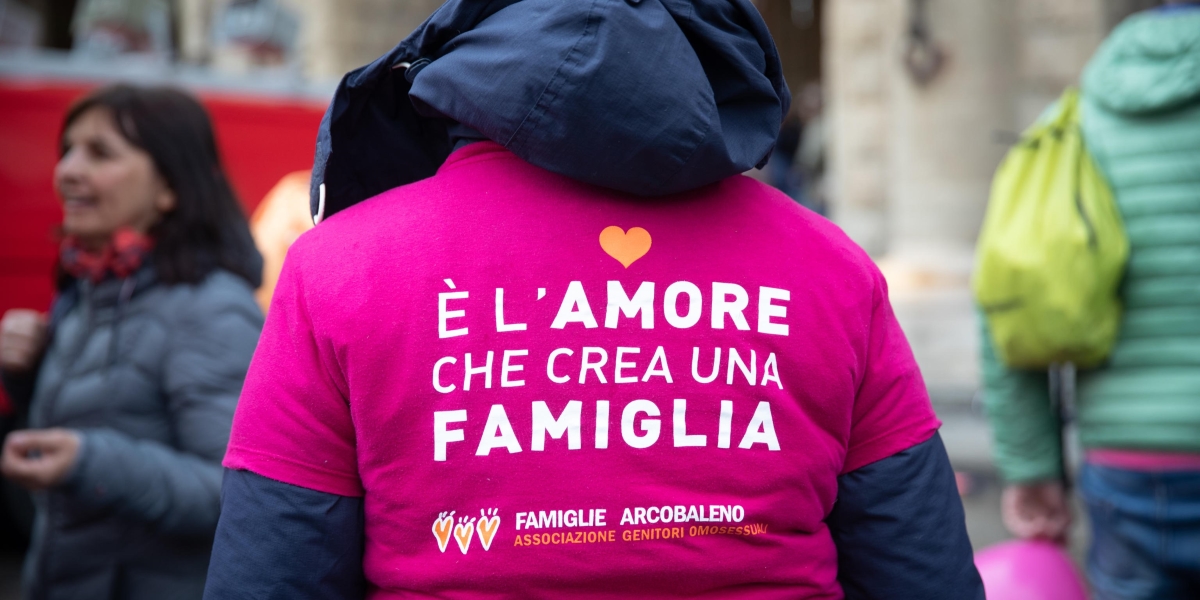 una persona di spalle indossa una maglietta con la scritta "è l'amore che crea una famiglia"