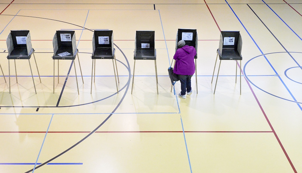 Una donna con un cappotto fucsia vota in una delle urne posizionate in fila al centro di una palestra