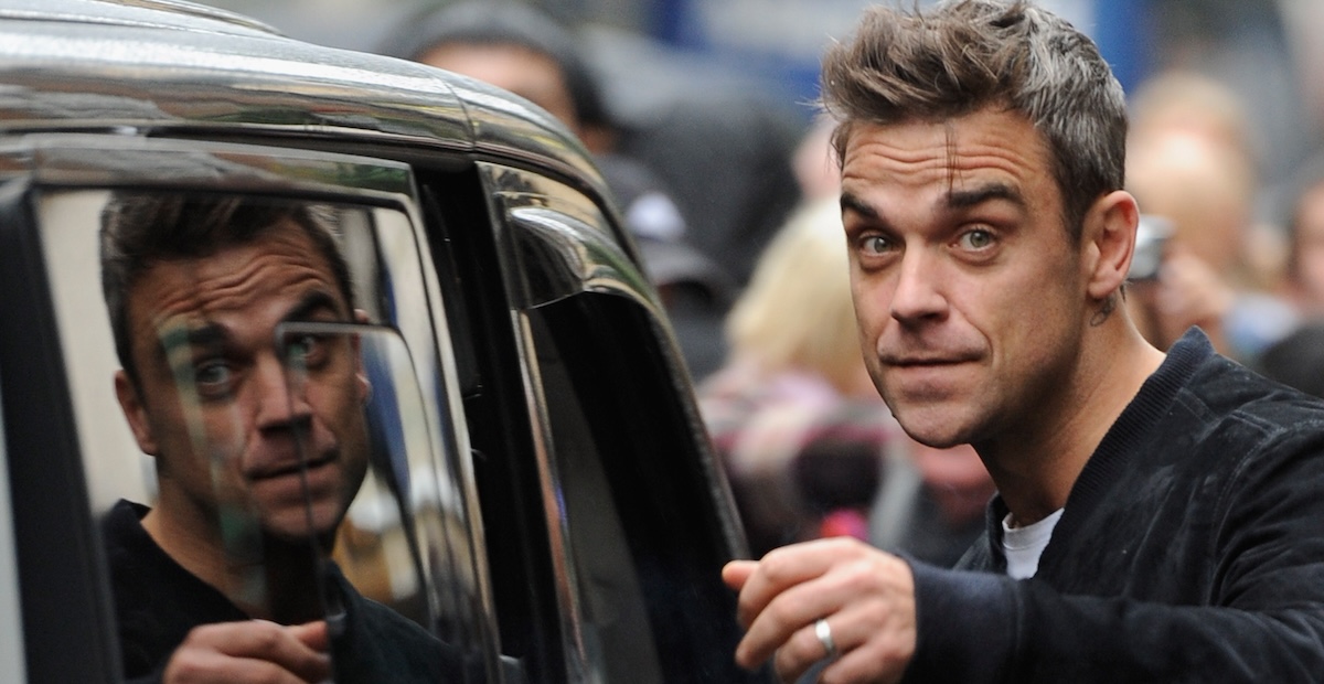 Robbie Williams guarda un fotografo mentre sale su un taxi in cui si vede la sua immagine riflessa