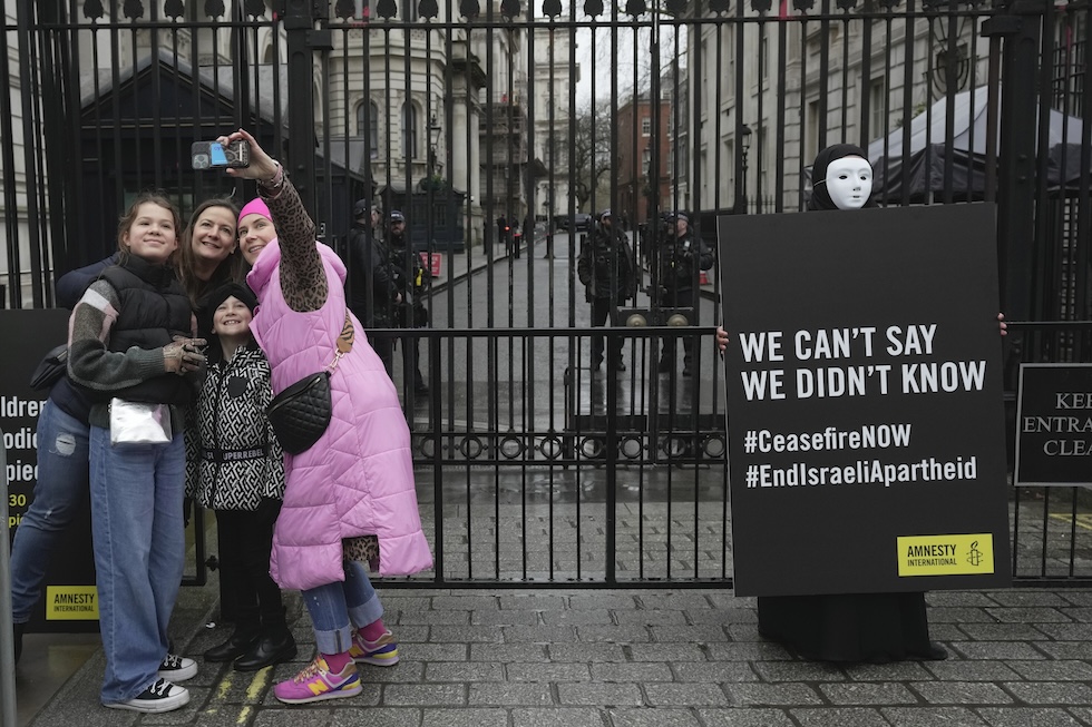 Quattro persone si scattano un selfie mentre un attivista di Amnesty International mostra un cartello di protesta contro gli attacchi israeliani nella Striscia di Gaza fuori da Downing street, la residenza del primo ministro britannico (Londra, Inghilterra)