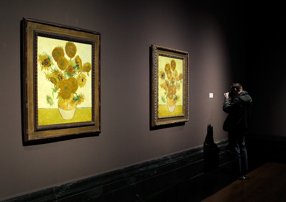 Un uomo scatta una fotografia con una reflex a uno di due dipinti molto simili che mostrano dei girasoli in un vaso