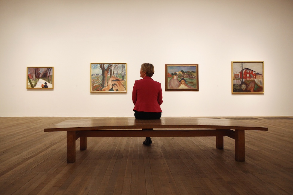Una donna seduta su una panchina al centro di una sala del museo, davanti a quattro dipinti