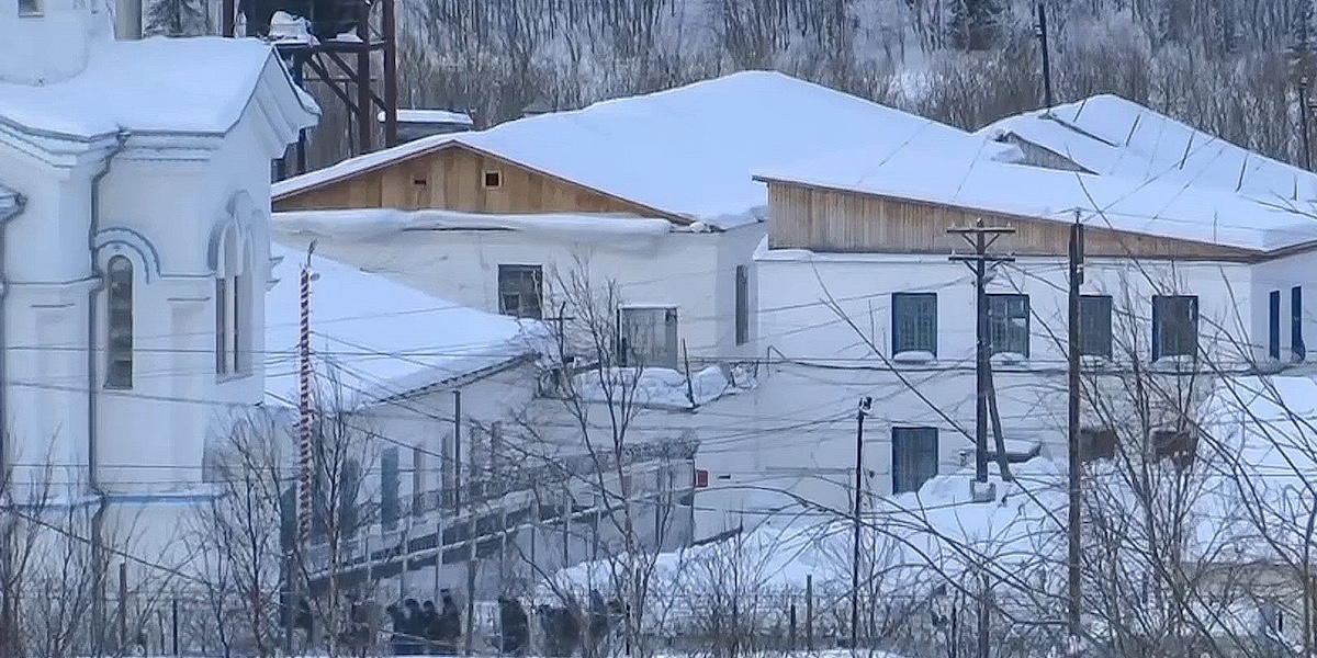 Un fermoimmagine di un video che mostra una parte della prigione di massima sicurezza in cui è morto Alexei Navalny. La foto mostra delle case con con dei tetti innevati, circondate da fili e telecamere.