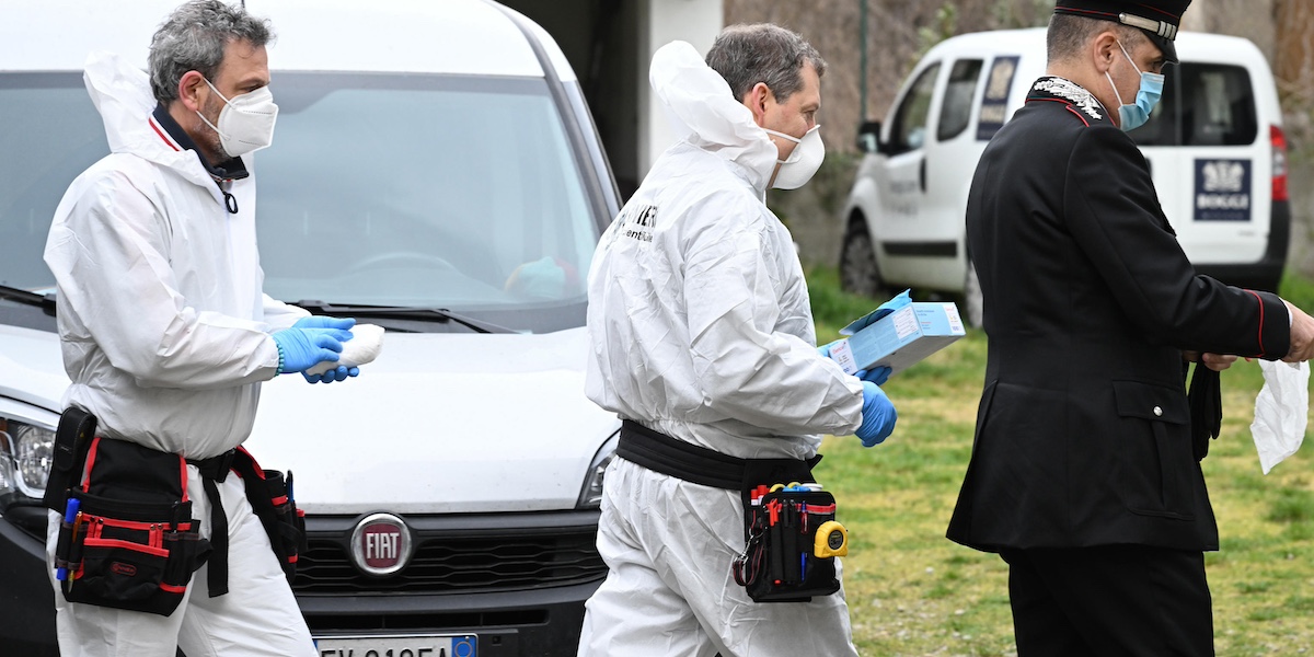 Due uomini in tuta bianca e un carabiniere camminano in fila indiana