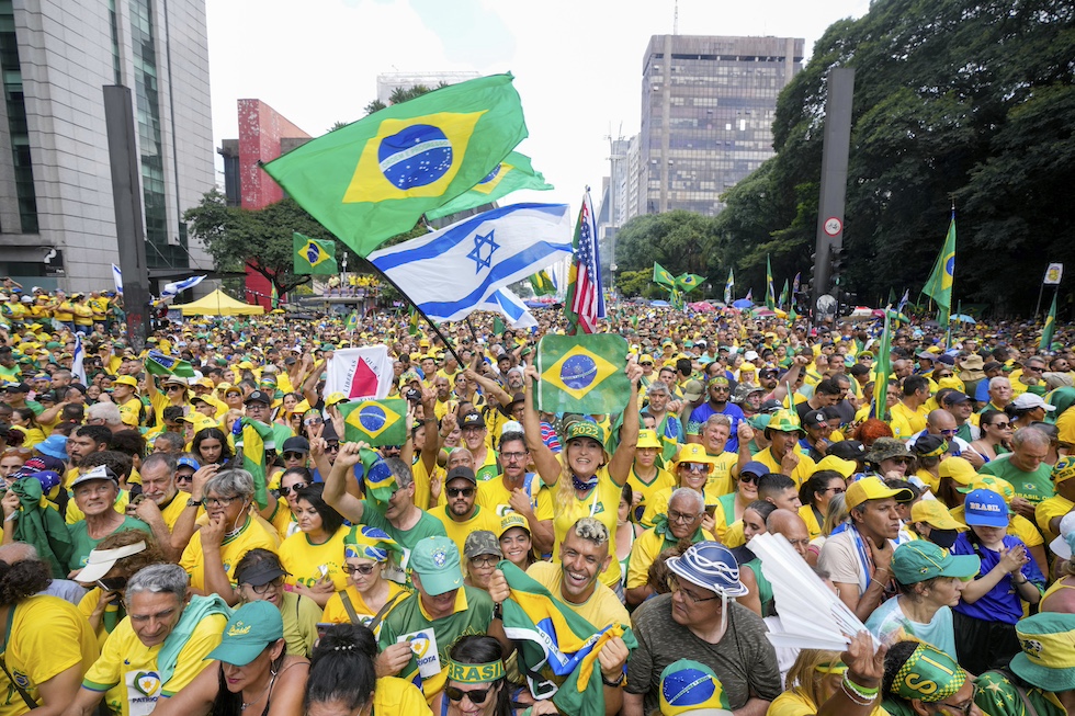 Foto della folla alla manifestazione con una bandiera del Brasile e una bandiera di Israele in primo piano