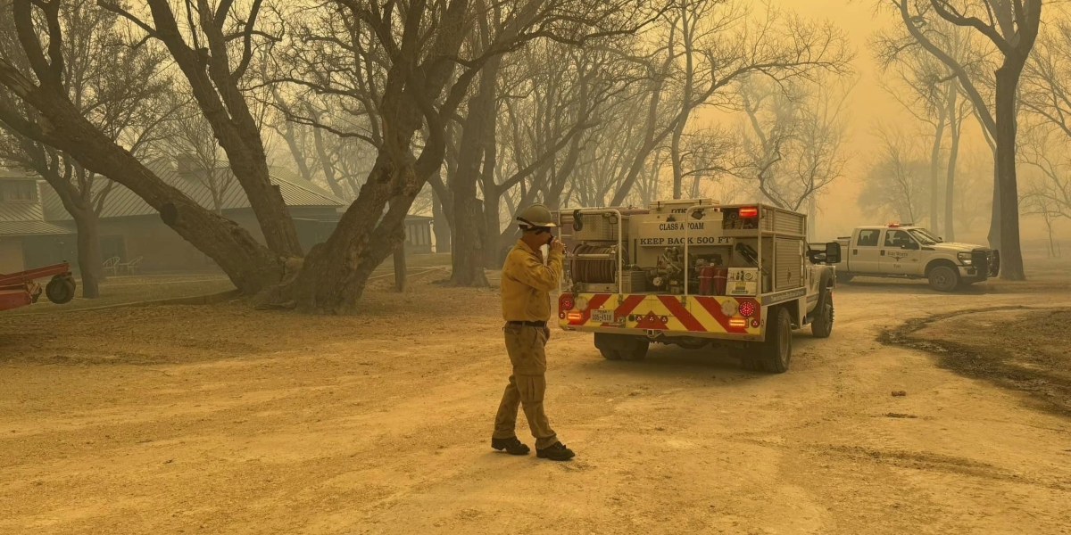 un vigile del fuoco e un camion dei vigili del fuoco in una zona interessata dagli incendi, con l'aria resa gialla dal fumo