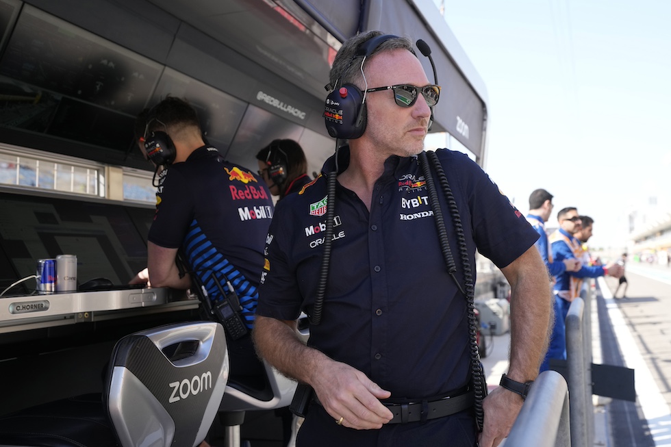 Christian Horner seduto al muretto della Red Bull, con gli occhiali da sole e le cuffie per parlare con i piloti, mentre si volta verso il garage