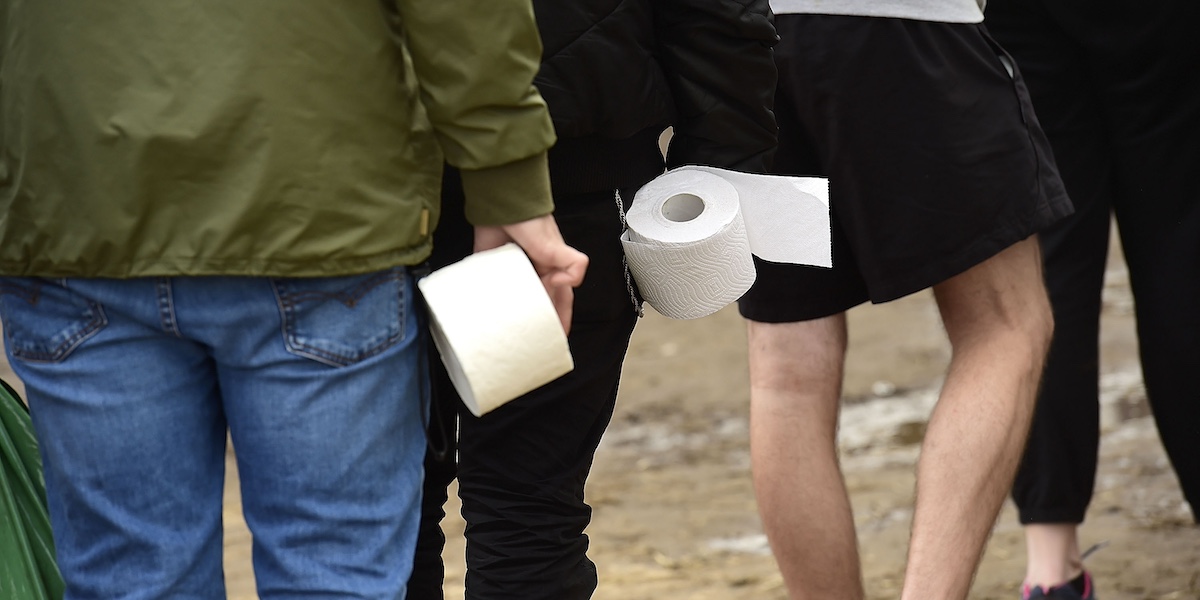 Un gruppo di persone in fila in un campeggio, ciascuna con un rotolo di carta igienica in mano