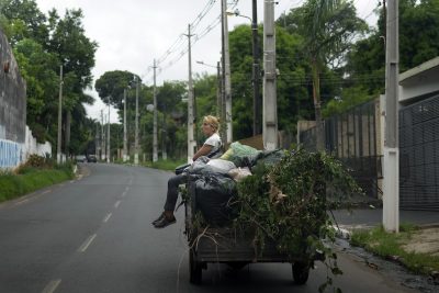 Una donna seduta tra rami degli alberi e sacchi di foglie su un motocarro guidato dal suo compagno, dopo aver lavorato nel giardino di una residenza privata