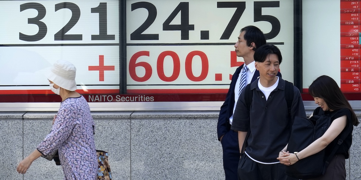 Alcune persone di fronte a un tabellone elettronico che mostra alcuni numeri relativi all'andamento dell'economia giapponese a Tokyo
