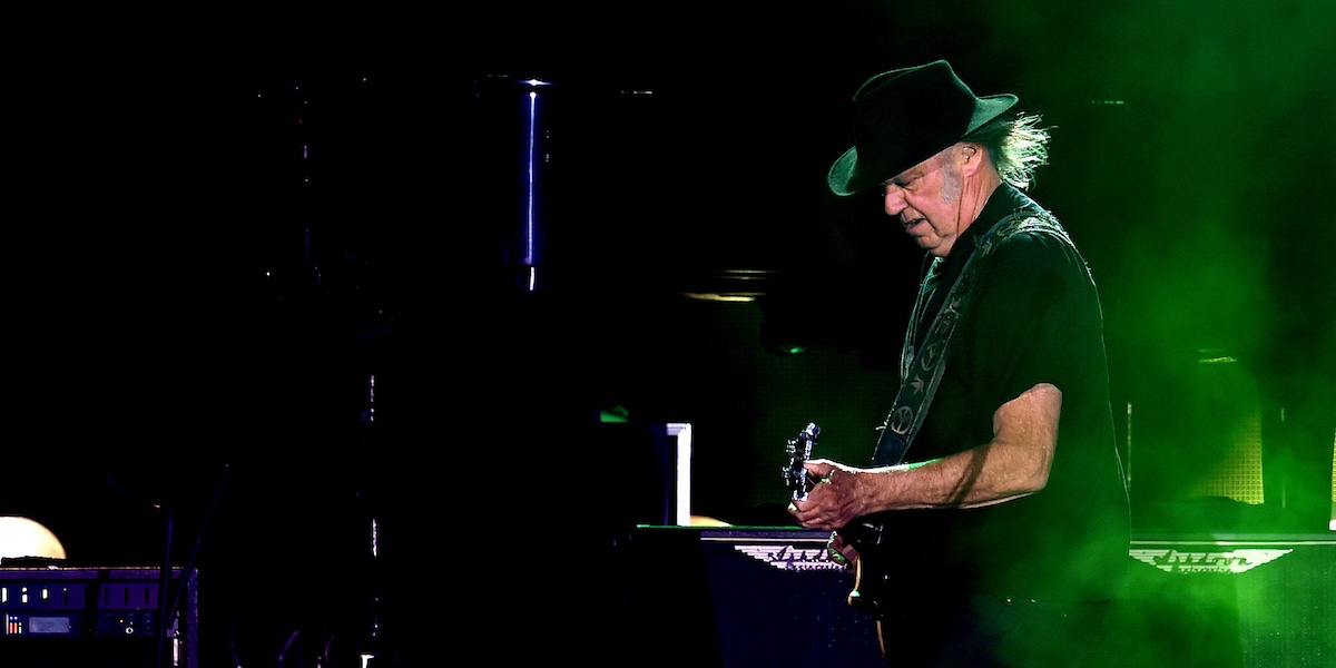 Neil Young che suona la chitarra di profilo su uno sfondo nero con una luce verde sulla destra