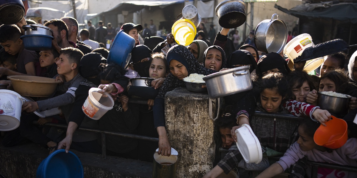 molti giovani palestinesi con dei contenitori in mano in attesa di ricevere del cibo
