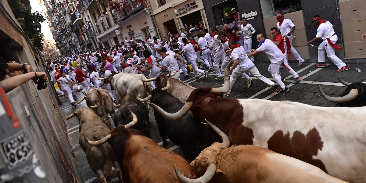 Una mandria di tori insegue un gruppo di uomini vestiti di bianco in un viottolo di un paese