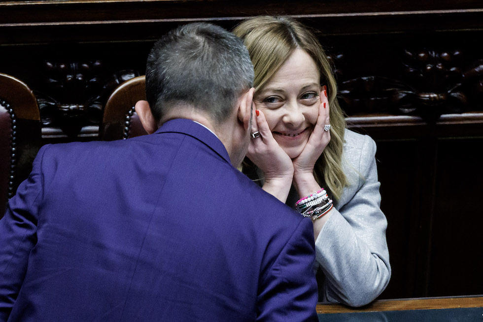 Foto di Meloni con il viso tra le mani e un sorriso sornione