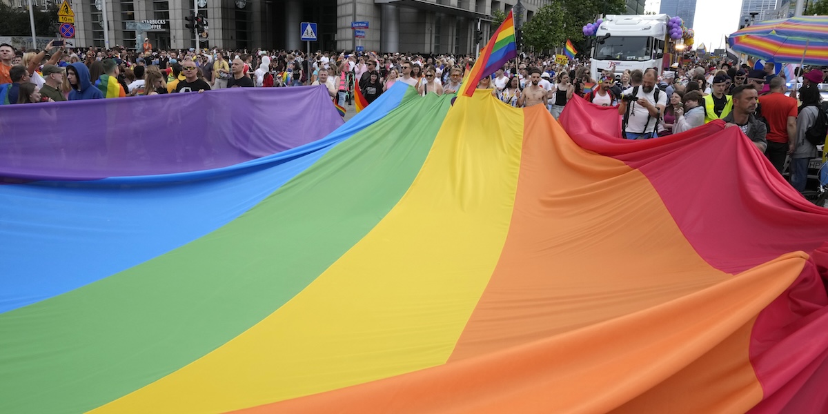 Persone sorreggono e stendono un grande telone coi colori arcobaleno durante una manifestazione a sostegno della comunità LGBT a Varsavia, in Polonia