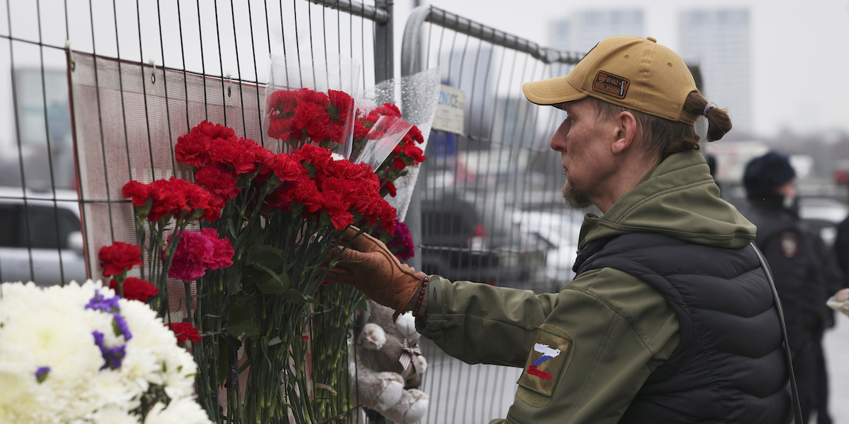 Foto di un uomo che posa fiori rossi sulla ringhiera fuori dal Crocus City Hall, a Mosca