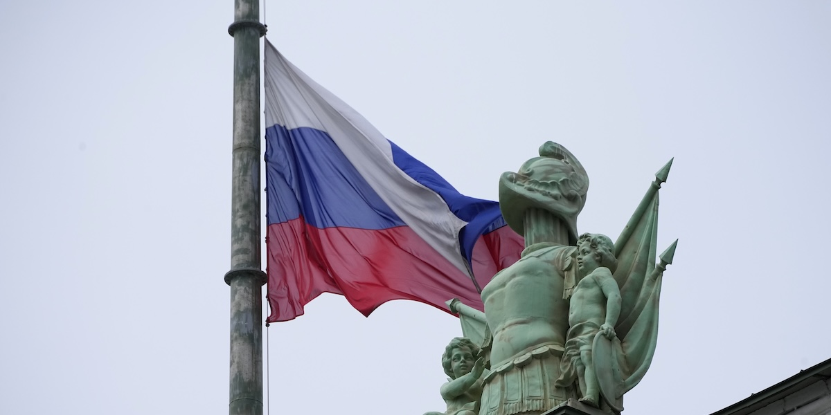 Una bandiera russa a mezz’asta vicino a una statua in cima a un edificio