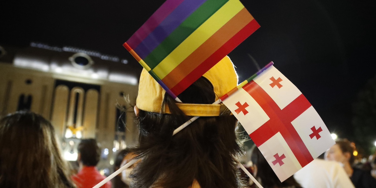 Una persona con un cappello in cui sono state infilate una bandierina arcobaleno e una bandierina con la bandiera della Georgia
