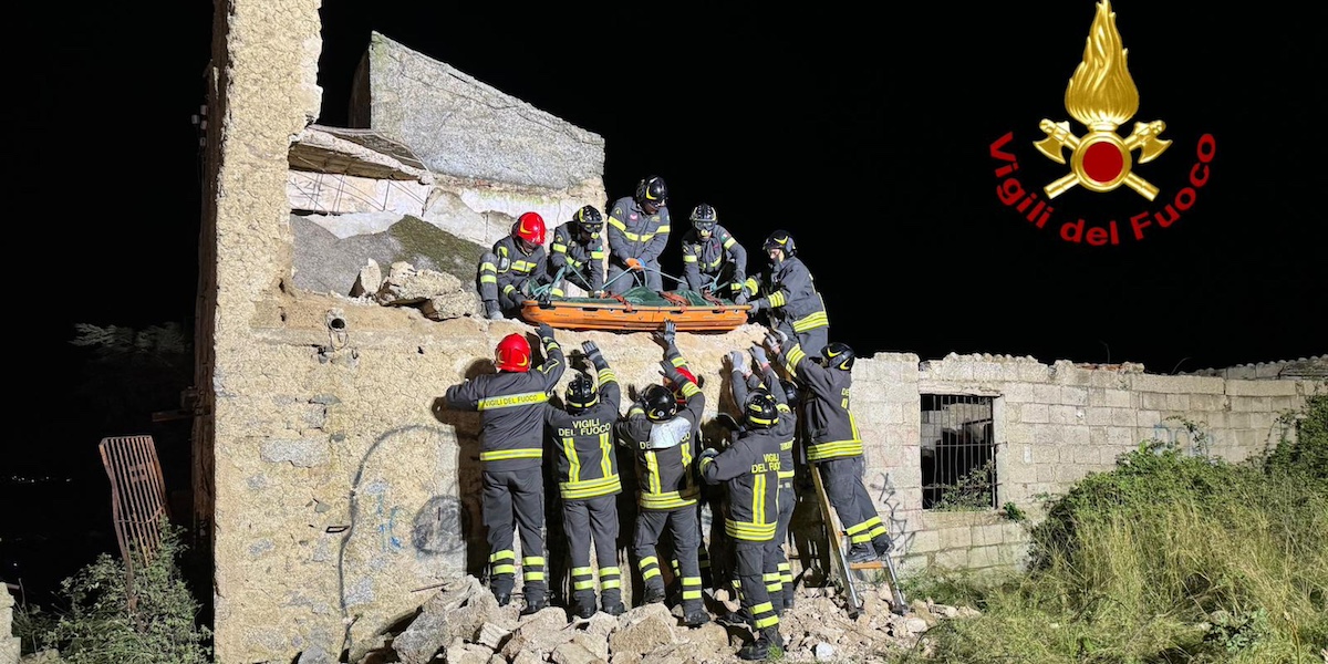 vigili del fuoco calano una barella dal piano superiore ad altri vigili del fuoco a terra, in una casa quasi completamente diroccata