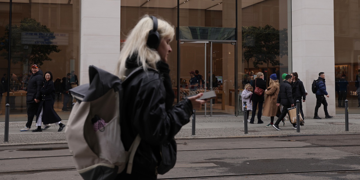 Una ragazza cammina lungo un marciapiede con lo sguardo sullo smartphone e le cuffie in testa