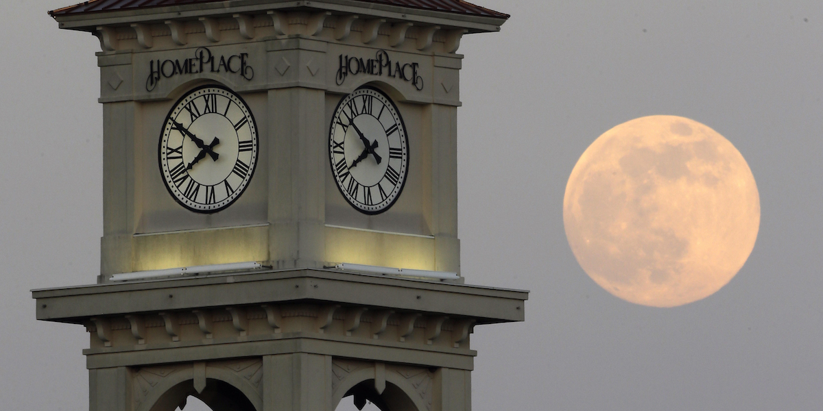Un orologio su una torre e la Luna visibile in cielo nello sfondo
