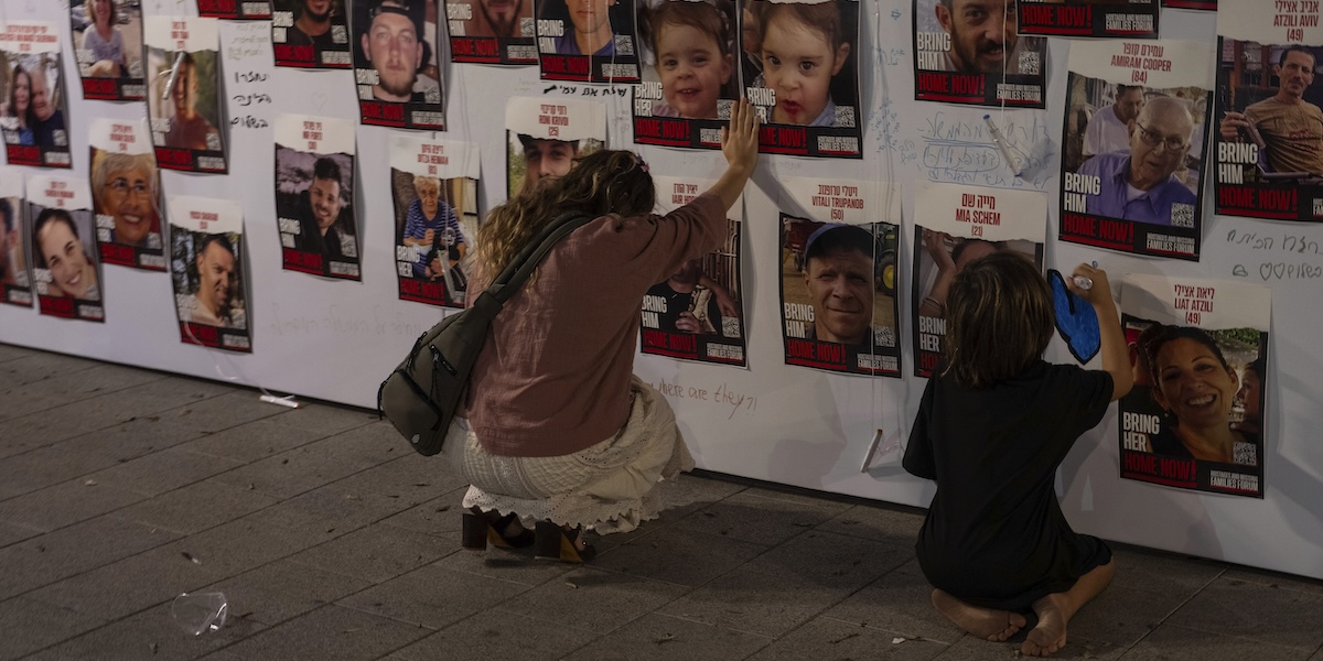 Una donna e un bambino inginocchiati di fronte ad alcune foto di ostaggi catturati da Hamas (AP Photo/Petros Giannakouris, File)
