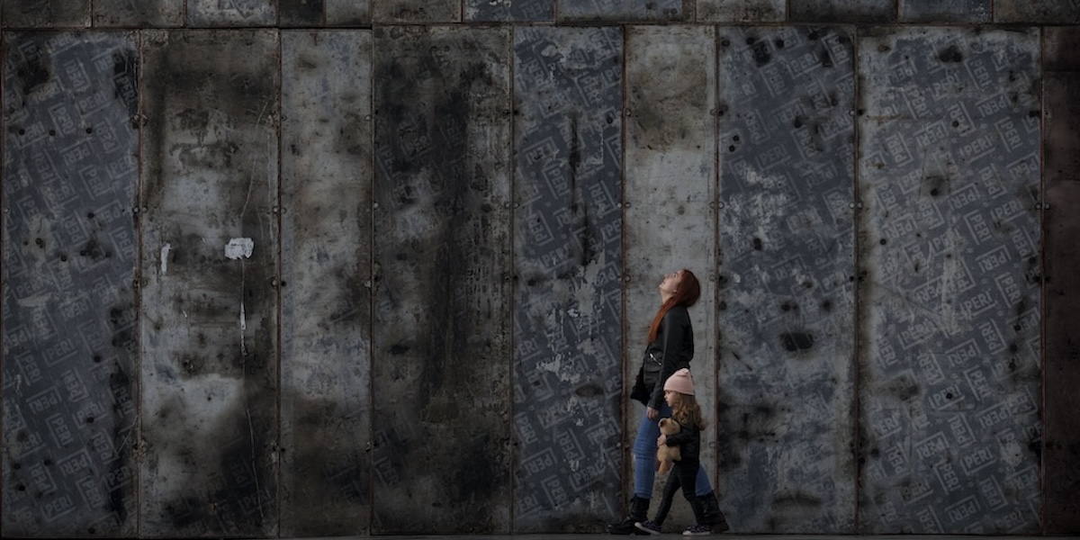 Una donna e un bambino camminano di fianco alle protezioni metalliche che coprono un monumento in un parco (AP Photo/Vadim Ghirda)