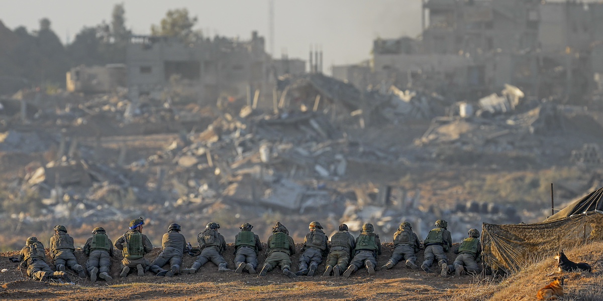 Soldati israeliani sdraiati a terra davanti a dei palazzi distrutti nella Striscia di Gaza a dicembre del 2023