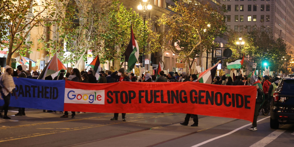 Una protesta di No Tech For Apartheid contro il Progetto Nimbus a San Francisco a dicembre del 2023. I manifestanti mostrano un grande striscione blu e rosso con scritto "google smetti di alimentare il genocidio"