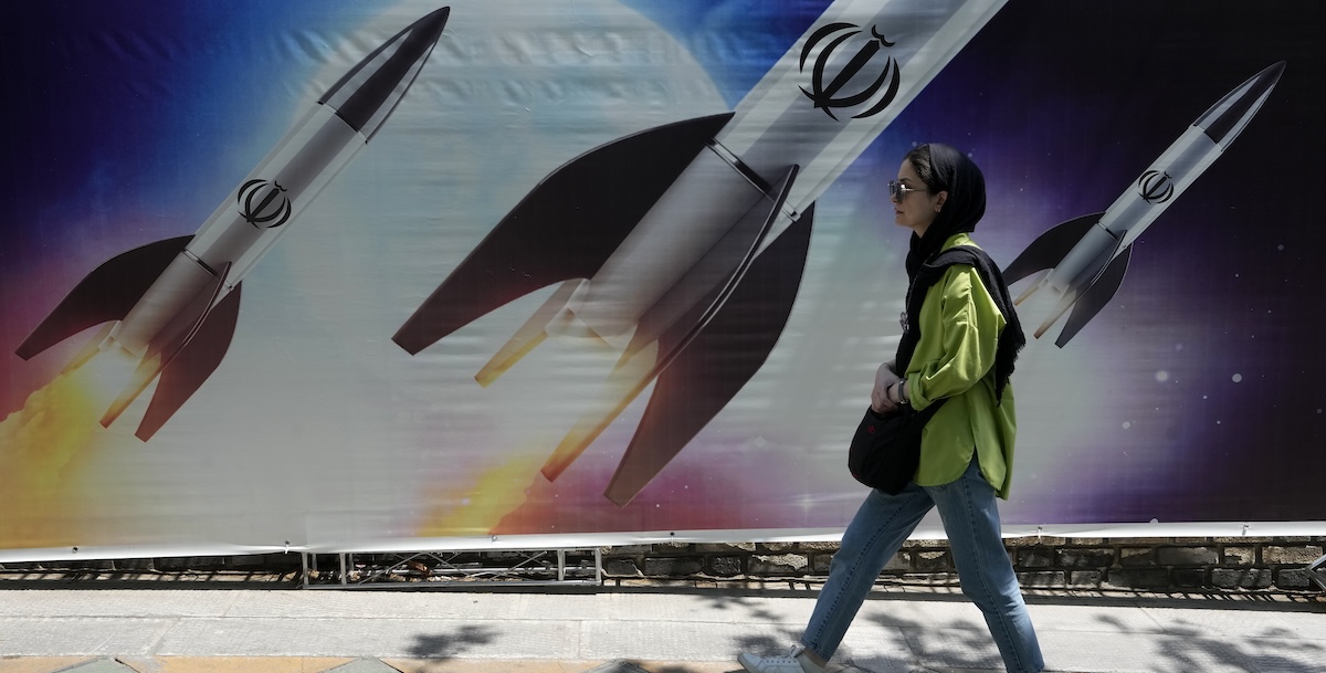 Una donna passa davanti a uno cartellone che mostra missili iraniani in fase di lancio, a Tehran (AP Photo/Vahid Salemi)