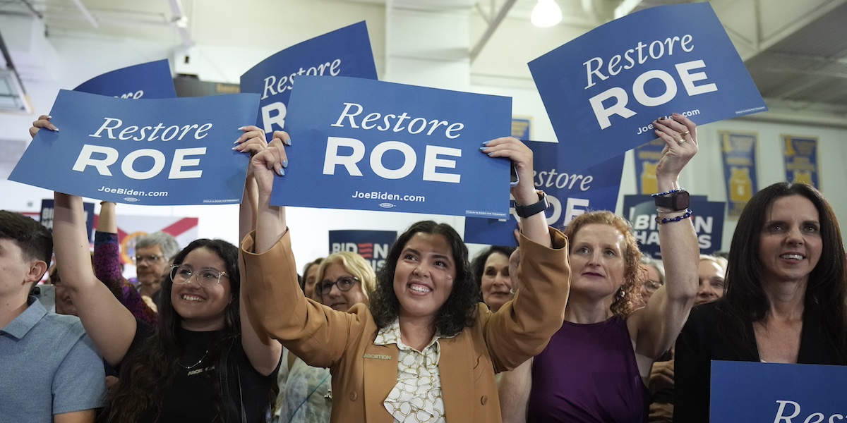 Donne con dei cartelli blu con su scritto "Ripristinare Roe", ossia la sentenza della Corte Suprema che legalizzava l'aborto a livello federale, annullata nel 2022, ad un comizio di Joe Biden a Tampa, in Florida