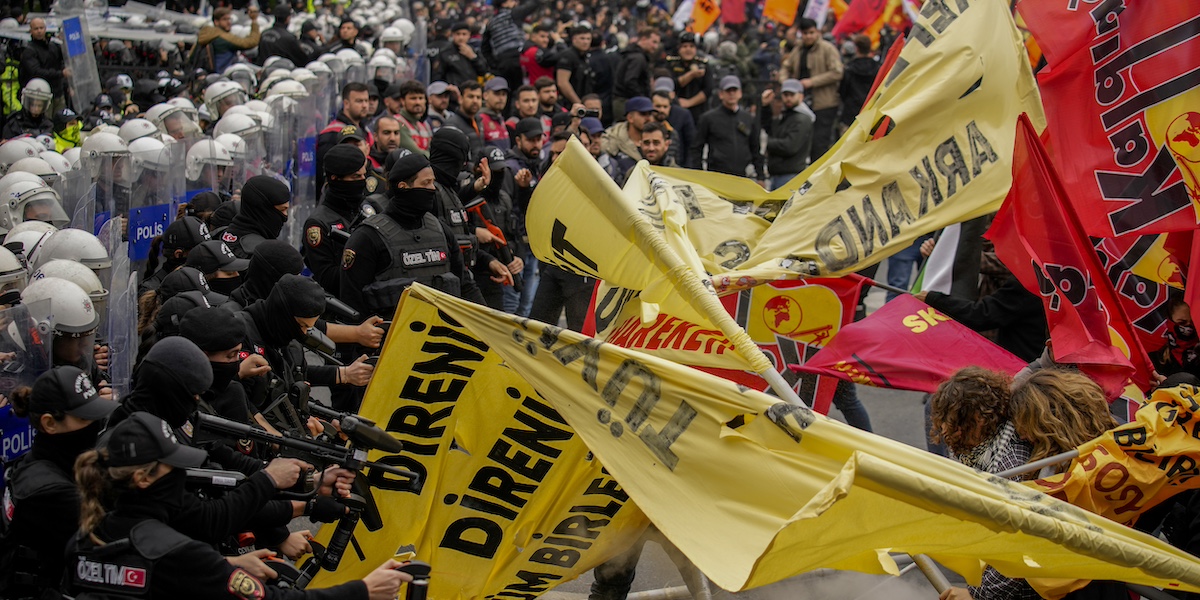 I manifestanti a destra, con striscioni gialli e rossi, si contrappongono alla polizia, a sinistra, con in mano fucili con proiettili di gomma