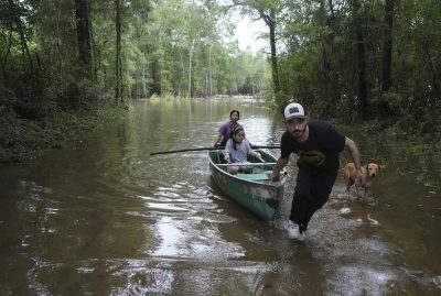 Un uomo spinge una canoa con a bordo una donna e una bambina in una zona allagata