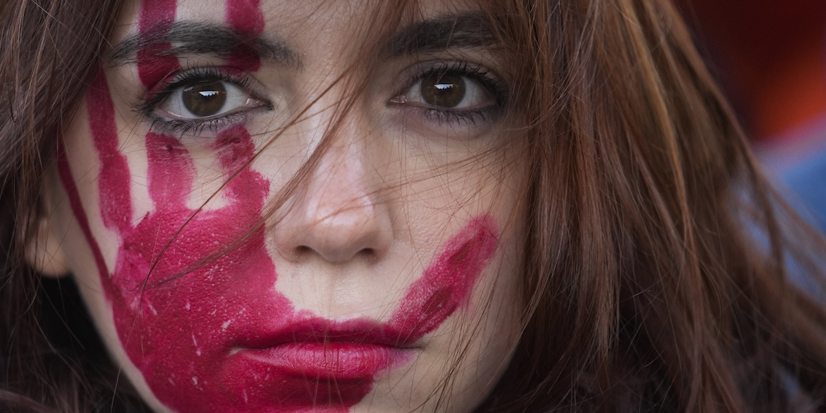 Il volto dipinto di rosso di una donna che manifesta contro la violenza sulle donne a Milano, il 25 novembre del 2023
