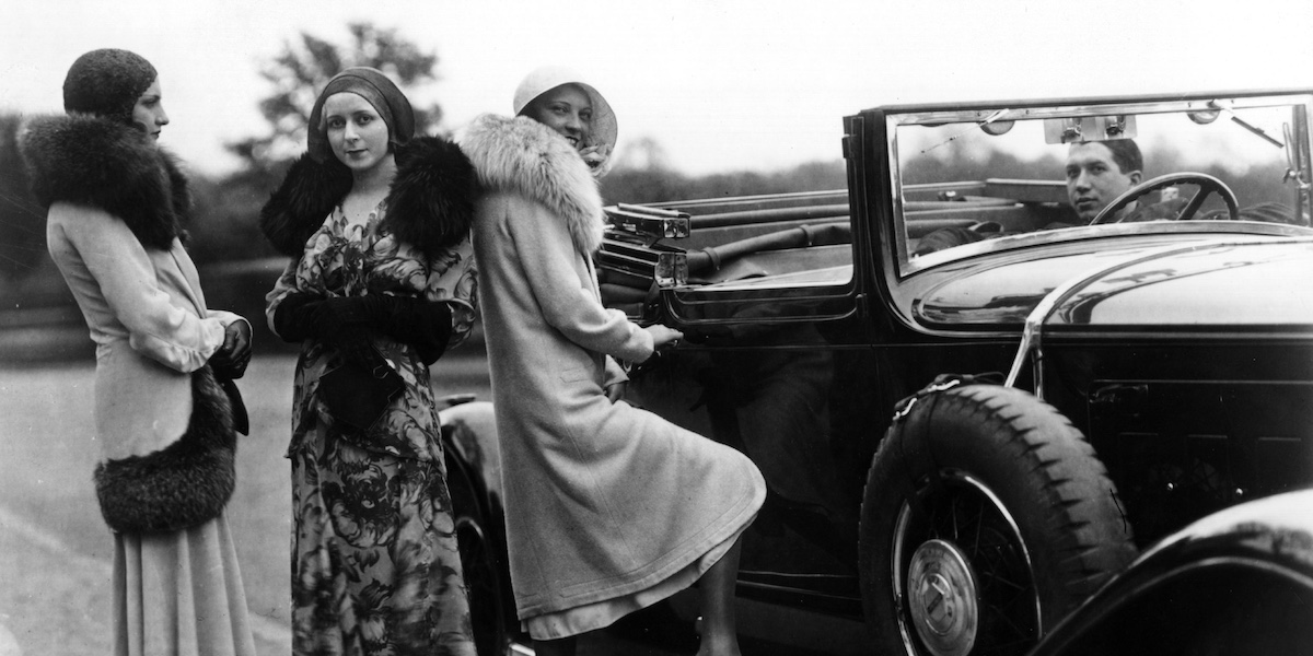 Una foto degli anni Venti che mostra tre donne con cappotti con collo in pelliccia vicino a un'auto cabriolet guidata da un uomo