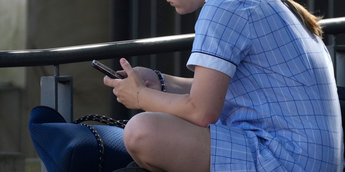 Una ragazzina usa il suo smartphone seduta su una panchina a Sydney, 8 novembre 2024 (AP Photo/Rick Rycroft)