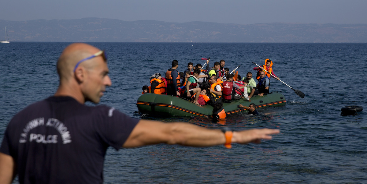 Un poliziotto greco davanti a un gommone con persone migranti, 2015