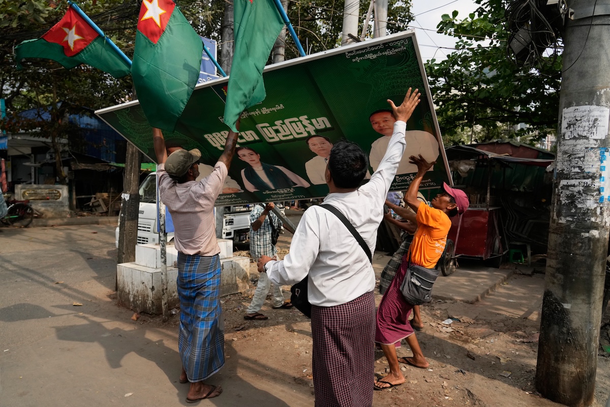 Membri del partito sostenuto dalla giunta militare rimuovono un cartellone pubblicitario elettorale a Yangon, in Myanmar, il 23 gennaio 2026 (AP Photo/Thein Zaw)