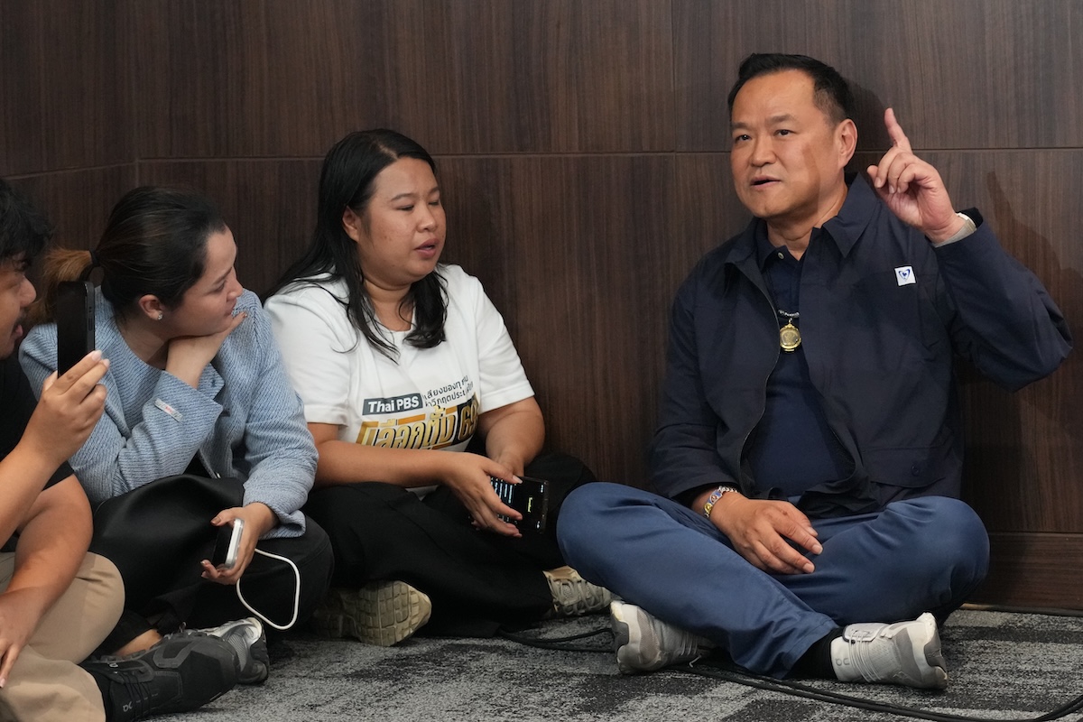 Il primo ministro uscente Anutin Charnvirakul, del partito Bhumjaithai, parla con i giornalisti seduto per terra, l'8 febbraio 2026 (AP Photo/Sakchai Lalit)